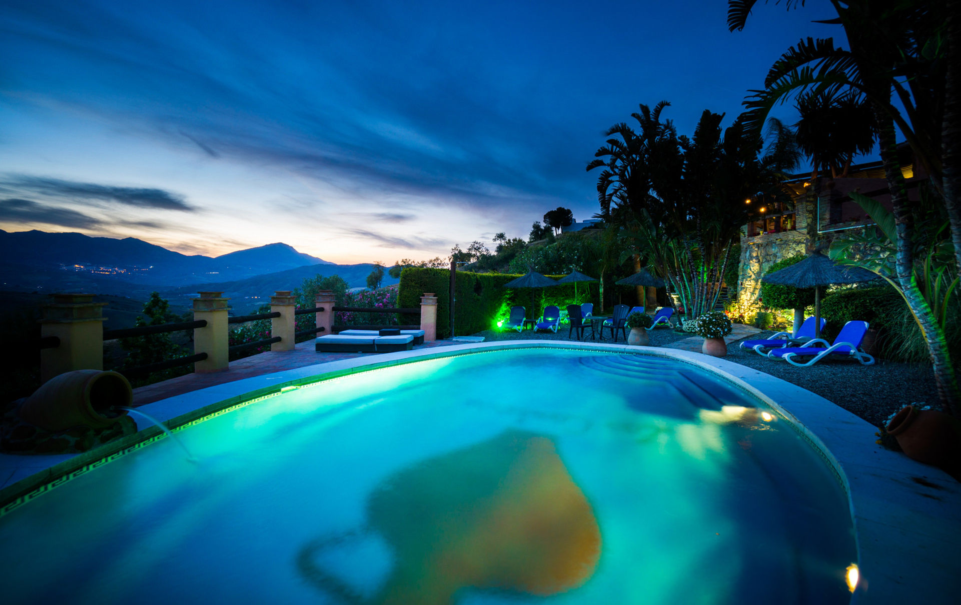 Vista de la piscina al anochecer, con iluminación en el jardín e impresionantes vistas del valle