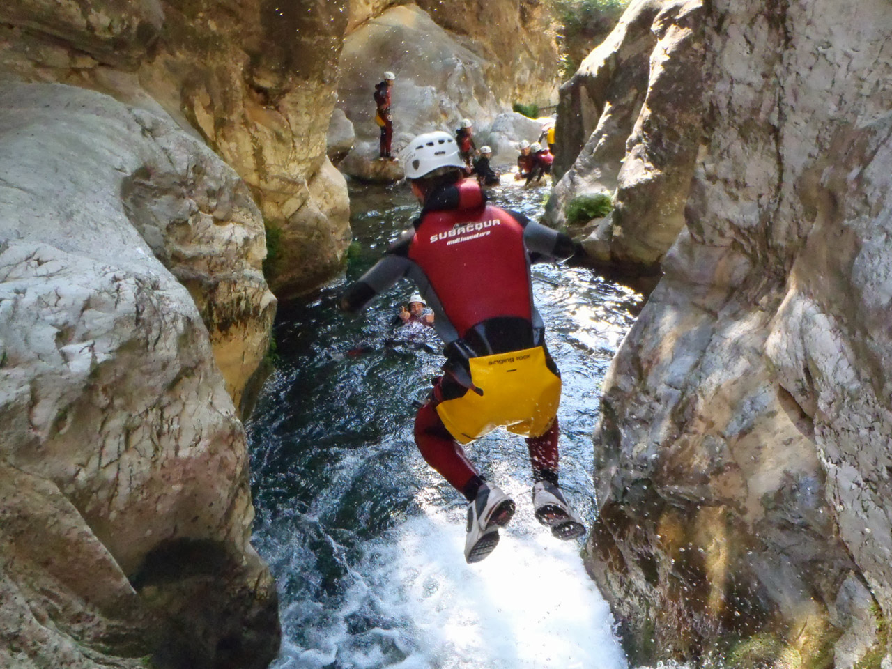 Varias personas debidamente equipadas haciendo barranquismo, una de ellas saltando a una poza de agua en un cañón rocoso