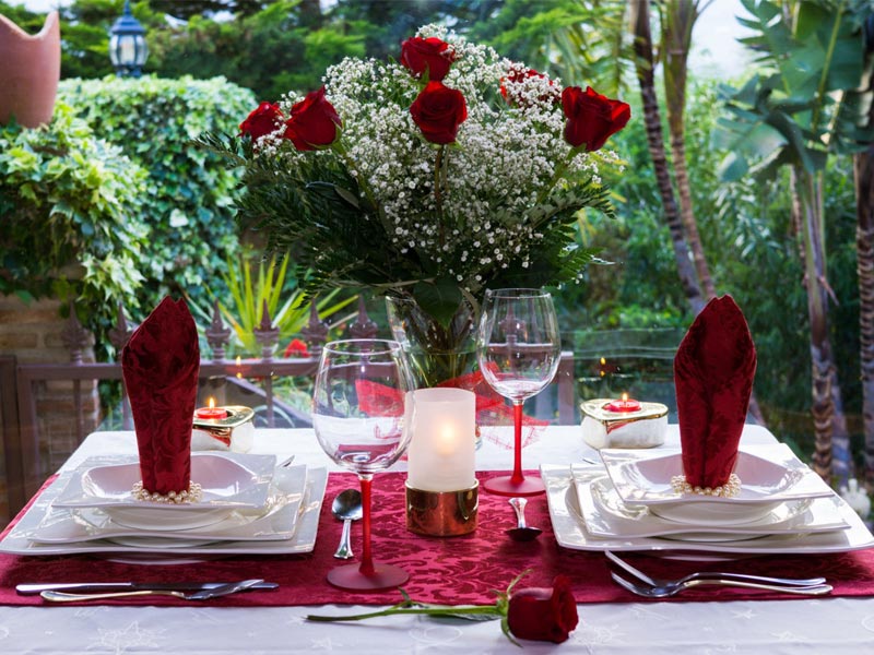 Mesa romántica para dos con ramo de rosas rojas y una rosa roja sobre el mantel