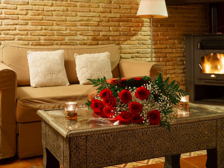 Detalle de mesa y sofá dentro de la habitación Jazmín SPA Exclusive, con velas y ramo de rosas, y la chimenea al fondo