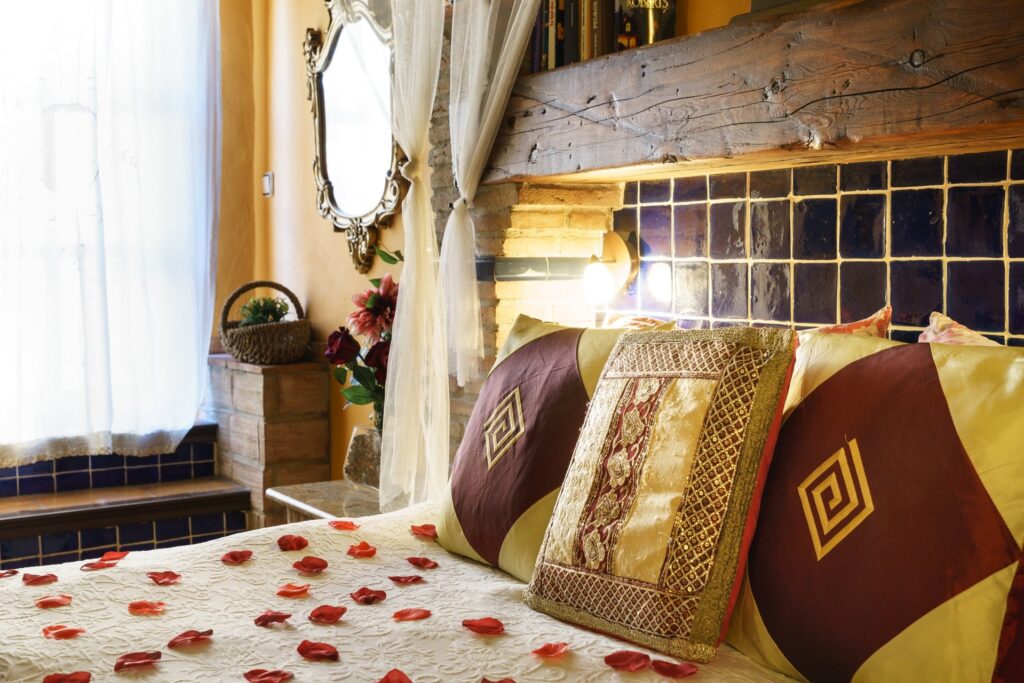 Cabecero de la cama de la habitación Orquídea Jacuzzi con imponente viga rústica, cojines, alicatado... y pétalos de rosa sobre la cama
