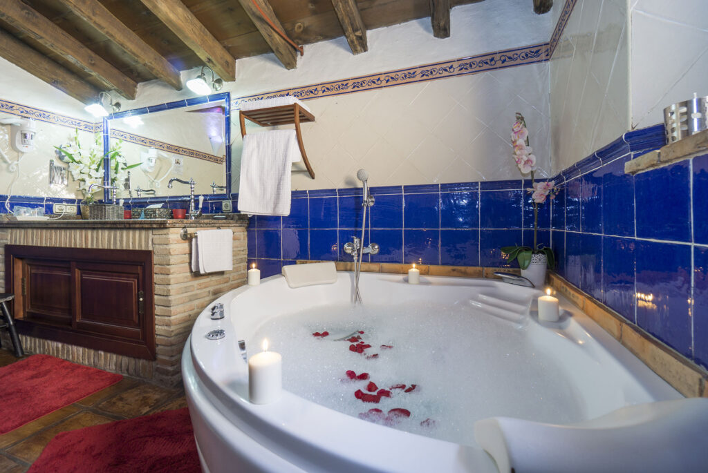Jacuzzi con espuma, pétalos de rosa y velas de la habitación Orquídea Jacuzzi. Al fondo el lavabo resto del baño en suite.