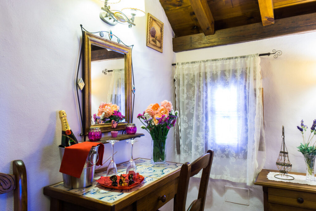 Espejo y mesa de la habitación Lavanda Romántica, con ramo de flores, champán enfriándose, copas, bombones y velas.