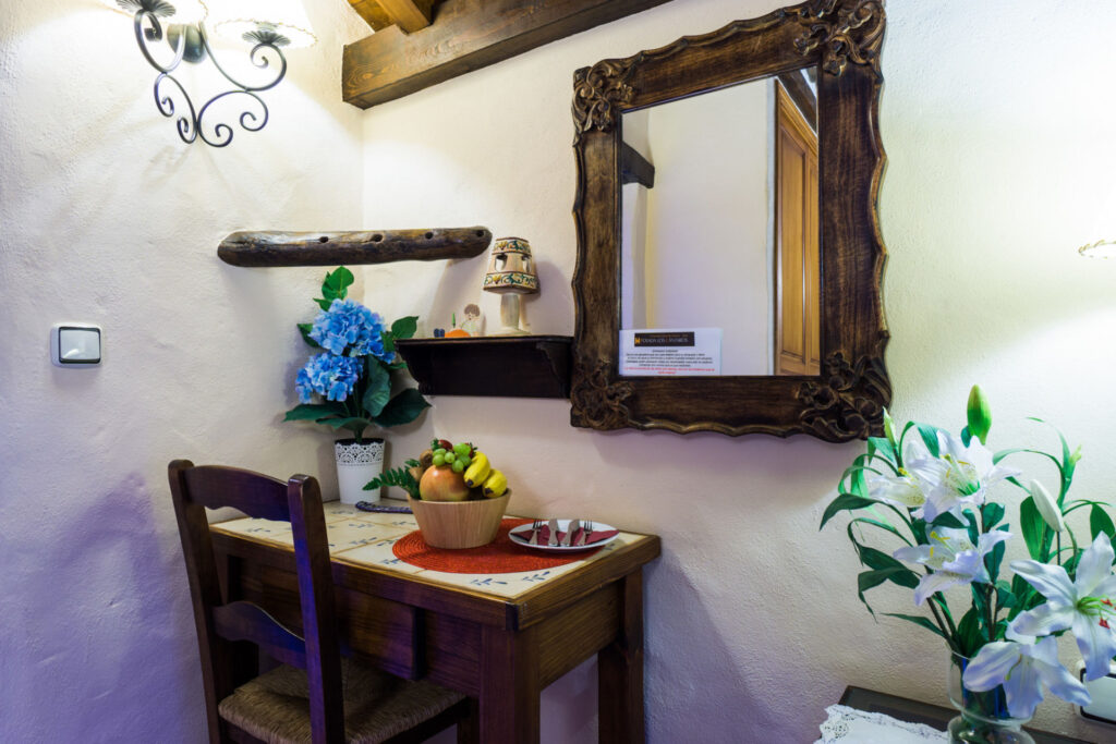 Espejo y mesa de la habitación Lilium Romántica, con ramo de flores, frutero con frutas y cubiertos