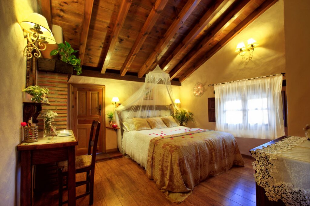 Vista general de la habitación Mimosa Jacuzzi, con cama con dosel y velo, pétalos de rosa esparcidos sobre la cama y resto del mobiliario y decoración