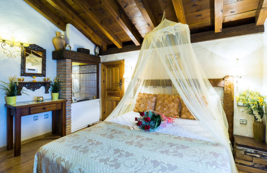 Vista general de la habitación Mimosa Jacuzzi, con cama con dosel y velo, ramo de flores sobre la cama y mobiliario