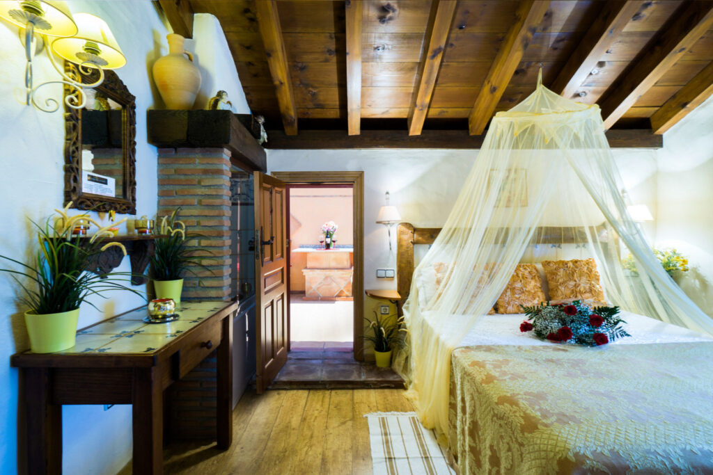 Cama con dosel y velo de la habitación Mimosa Jacuzzi, con ramo de flores sobre la cama, acceso al baño en suite y mobiliario