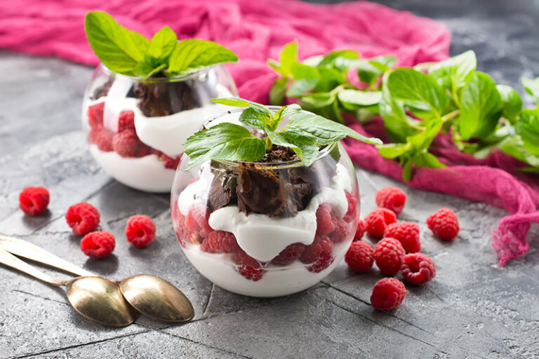 Dos postres de frambuesas con yogurt, presentados en bol de cristal transparente y adornado con hierbas y frambuesas