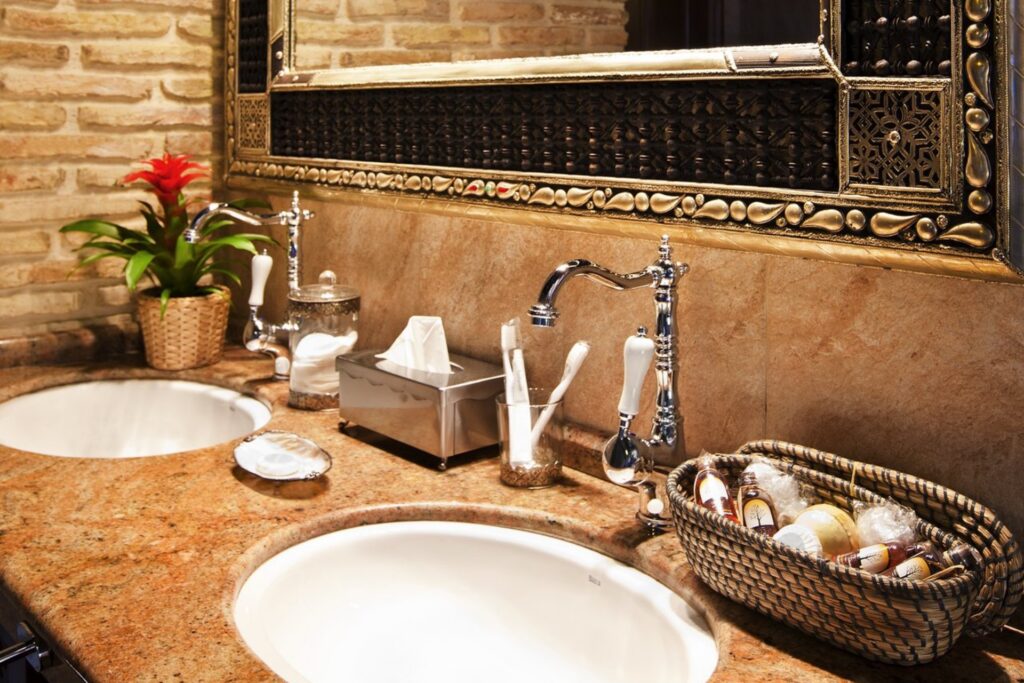 Detalles del baño de la habitación Jazmín SPA Exclusive, con dos lavabos, espejo, grifos de diseño, todos los enseres y cesta con esencias