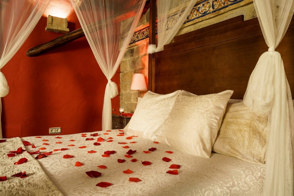 Cama de la habitación Jazmín SPA Exclusive, con dosel y velo, y pétalos de rosa esparcidos sobre la cama