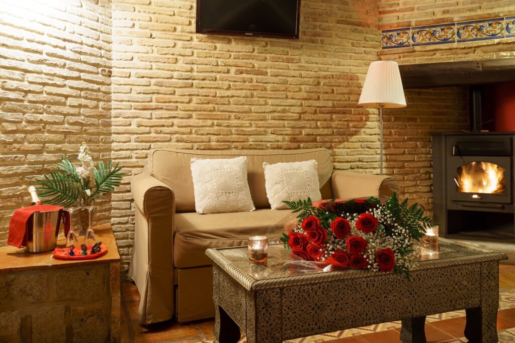 Detalle de mesa y sofá dentro de la habitación Jazmín SPA Exclusive, con velas y ramo de rosas, y la chimenea al fondo